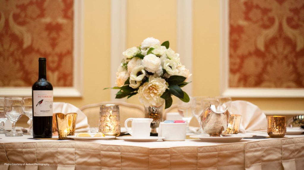 Head Table setting with floral arrangement, silver tableware, and a bottle of wine.