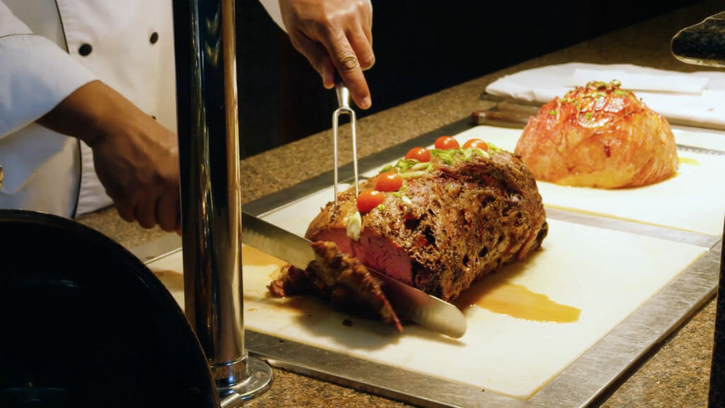 Chef cutting a large piece of meat behind a buffet line.