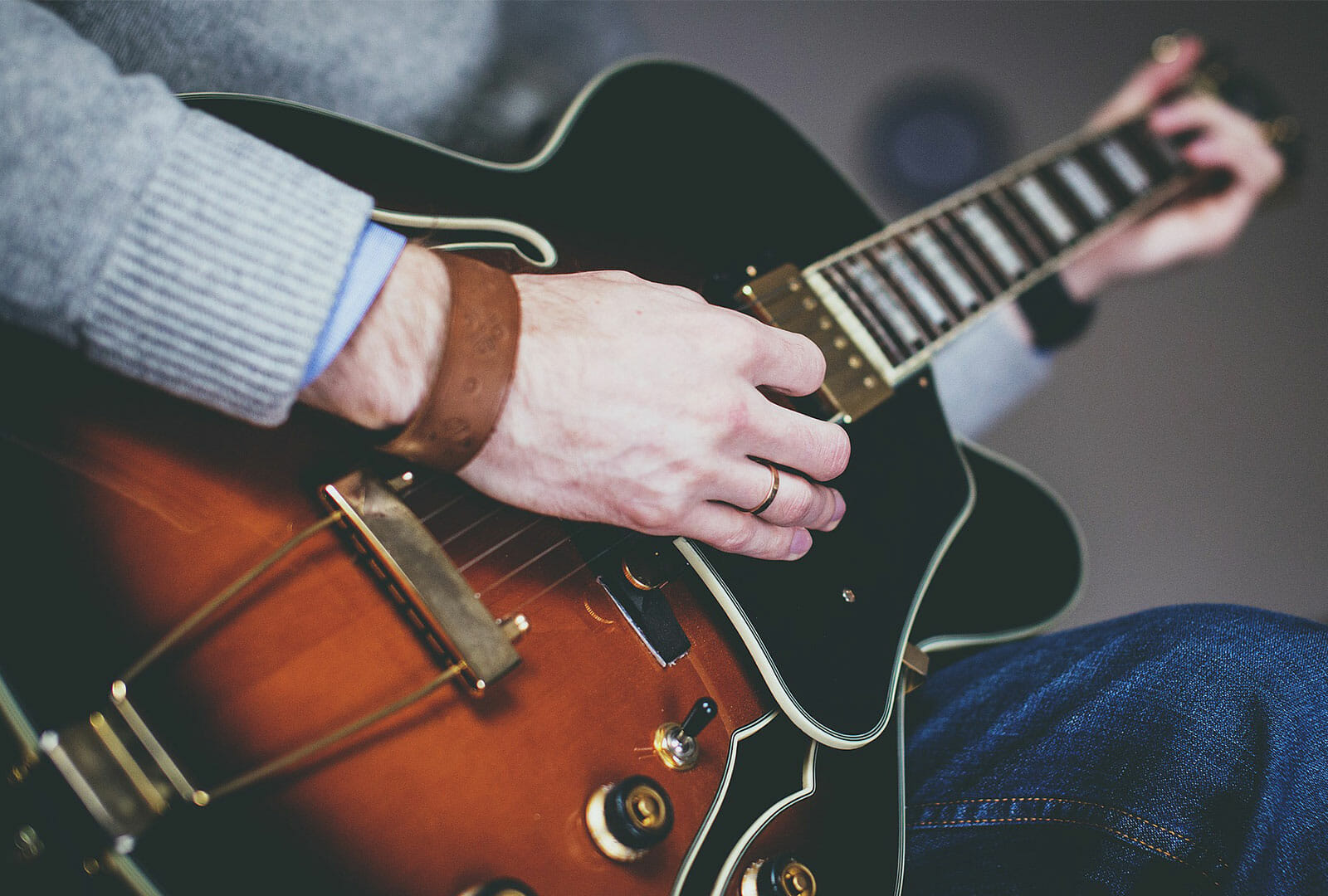 Close up of man playing electric guitar wearing a gray sweater