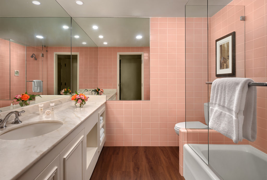 Pink bathroom with shower, tub, and marble counters with flowers on the counter.