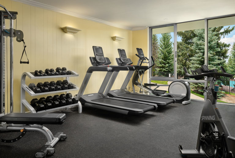 Fitness Center with three treadmills, free weights, and a stationary bike with big windows looking outside.