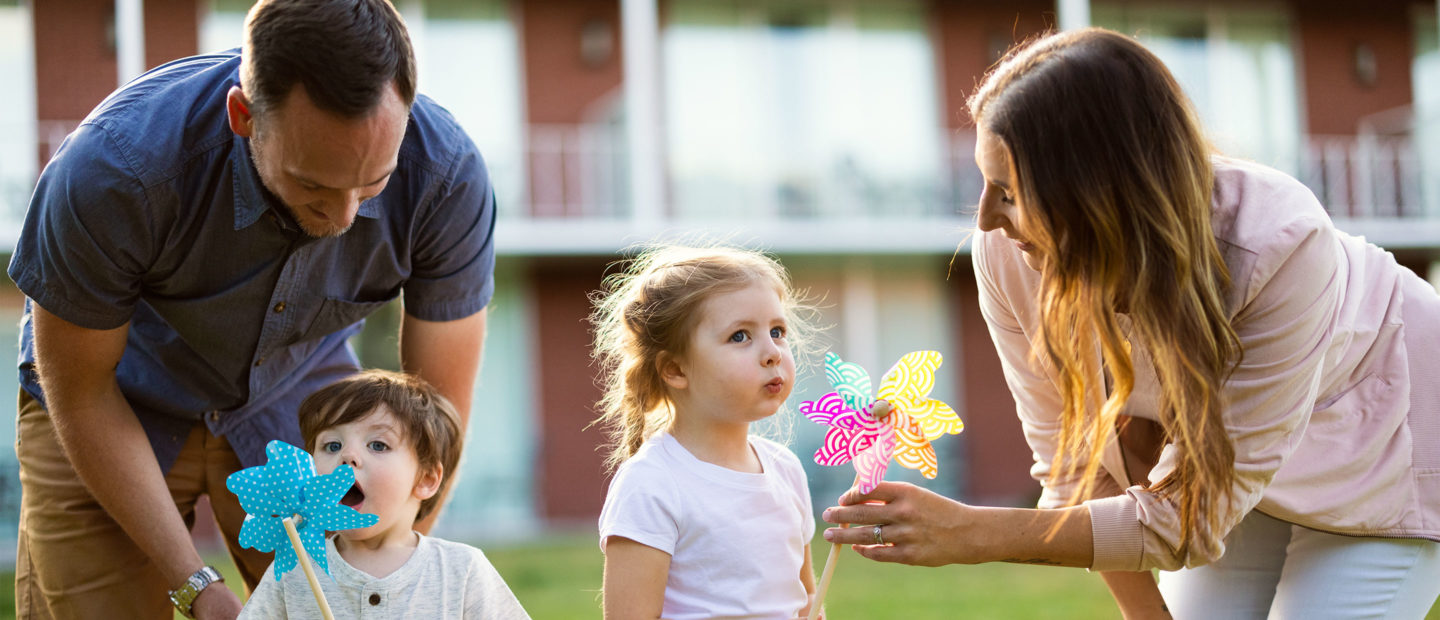 Photo of parents with two young children, a boy and a girl, playing with pinwheels.