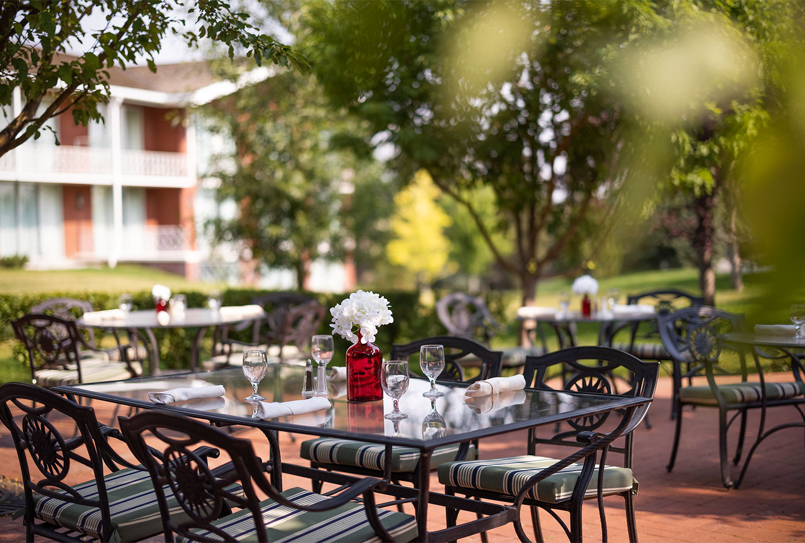 Glass table with water glasses and silverware bundles set with the lodges blurred in the background on Hathaway's outdoor patio.