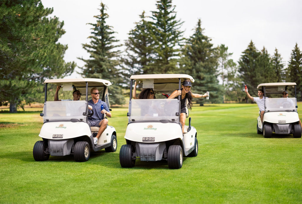 Three golf carts with a group of 6 friends spread out between them driving on the golf course.