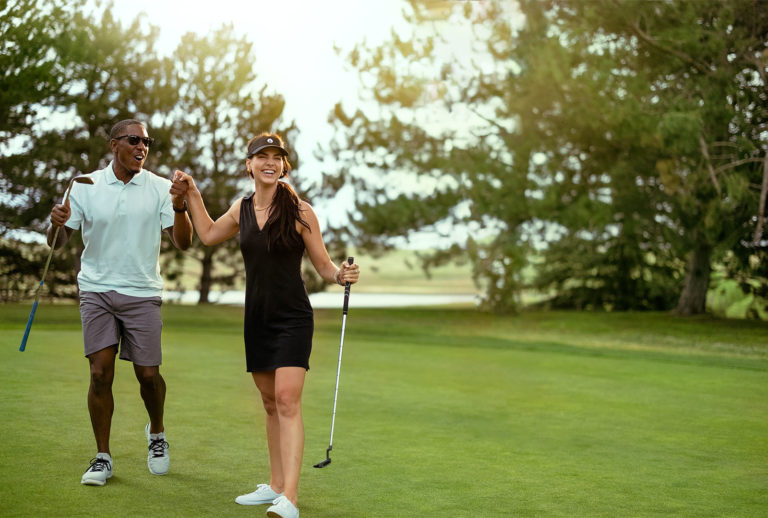 A couple holding hands walking with golf clubs celebrating a good shot on a golf course.