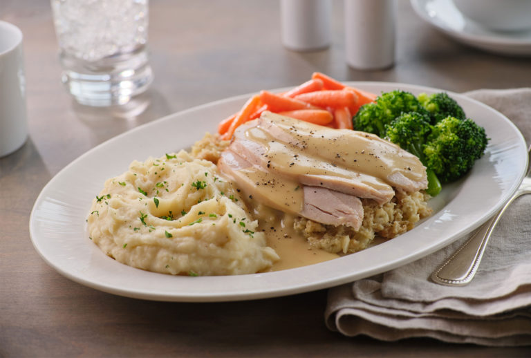 Close up of a plate of turkey, mashed potatoes, stuffing, and veggetables.