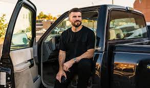 Picture of Sam Hunt sitting in the front doorway of a truck.